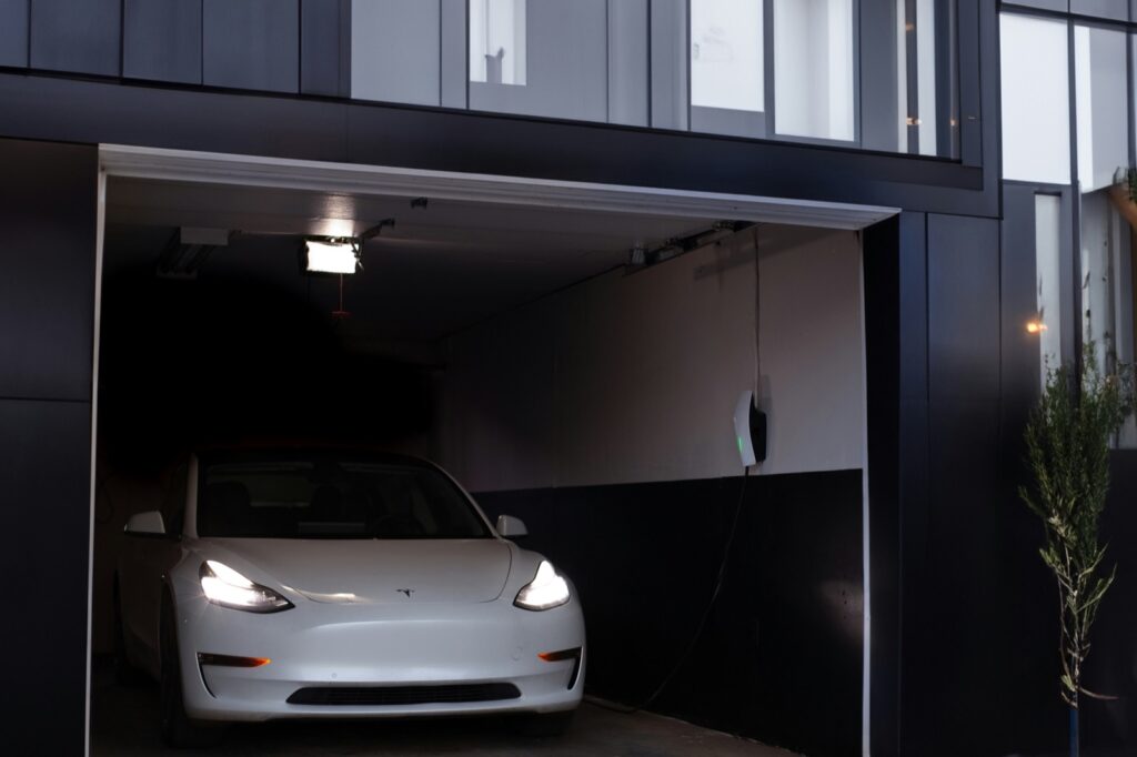 Tesla charging from a wall connector in a home garage at dusk